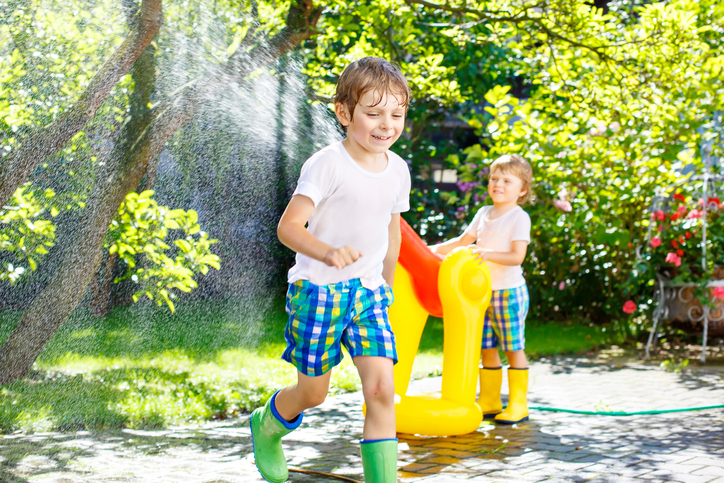Two little kids boys playing with a garden hose water sprinkler